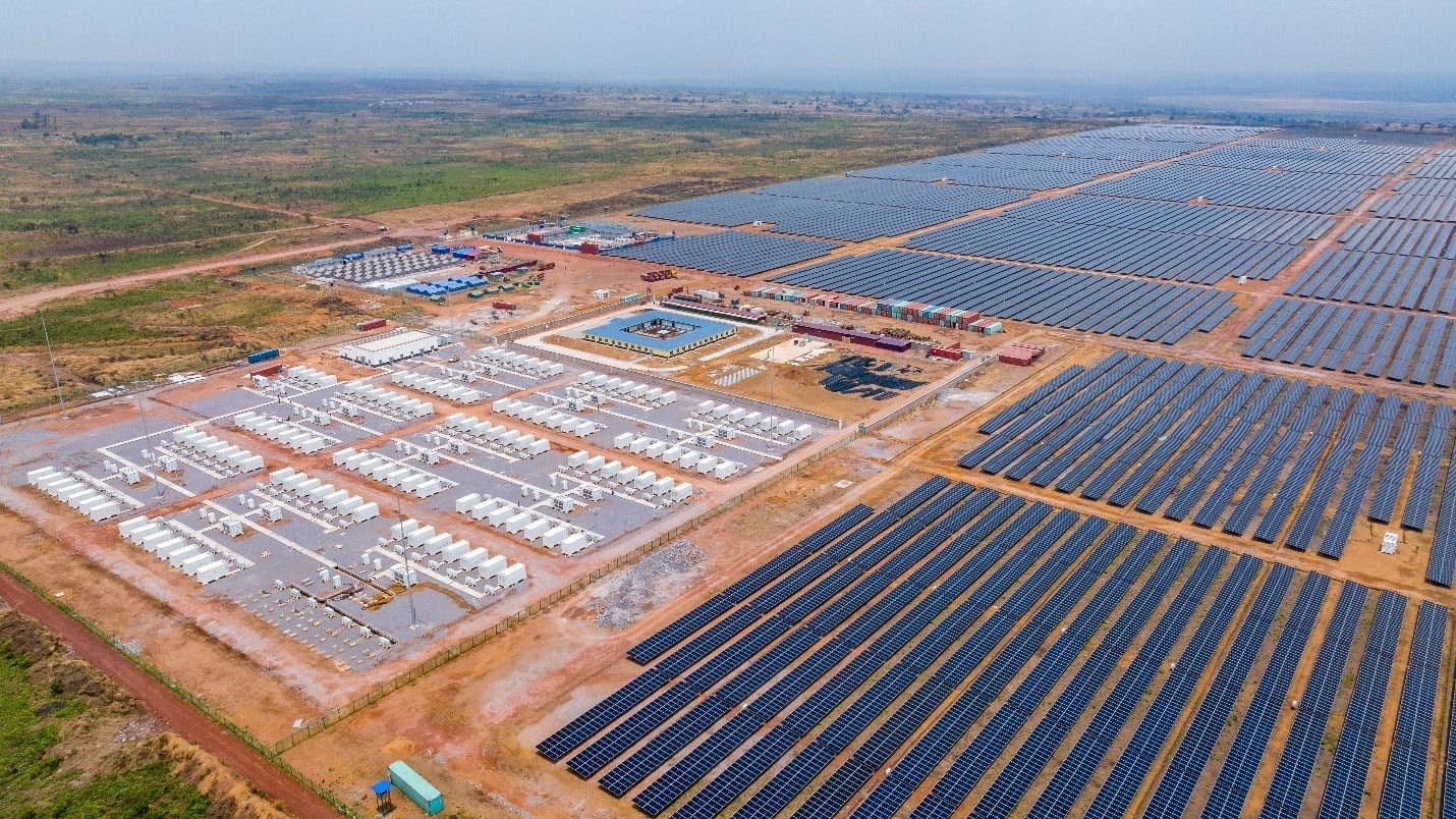 An aerial photograph shows rows of solar panels and a few buildings across open terrain.