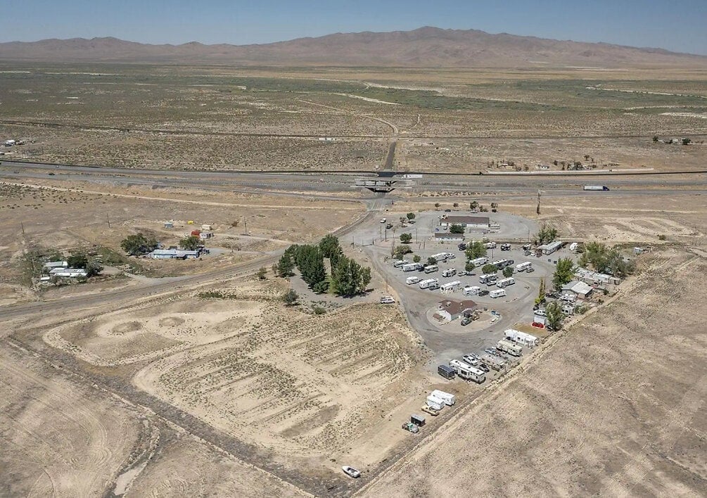 An aerial view shows an RV park amid arid terrain, with buildings, trailers and mountains in the background.