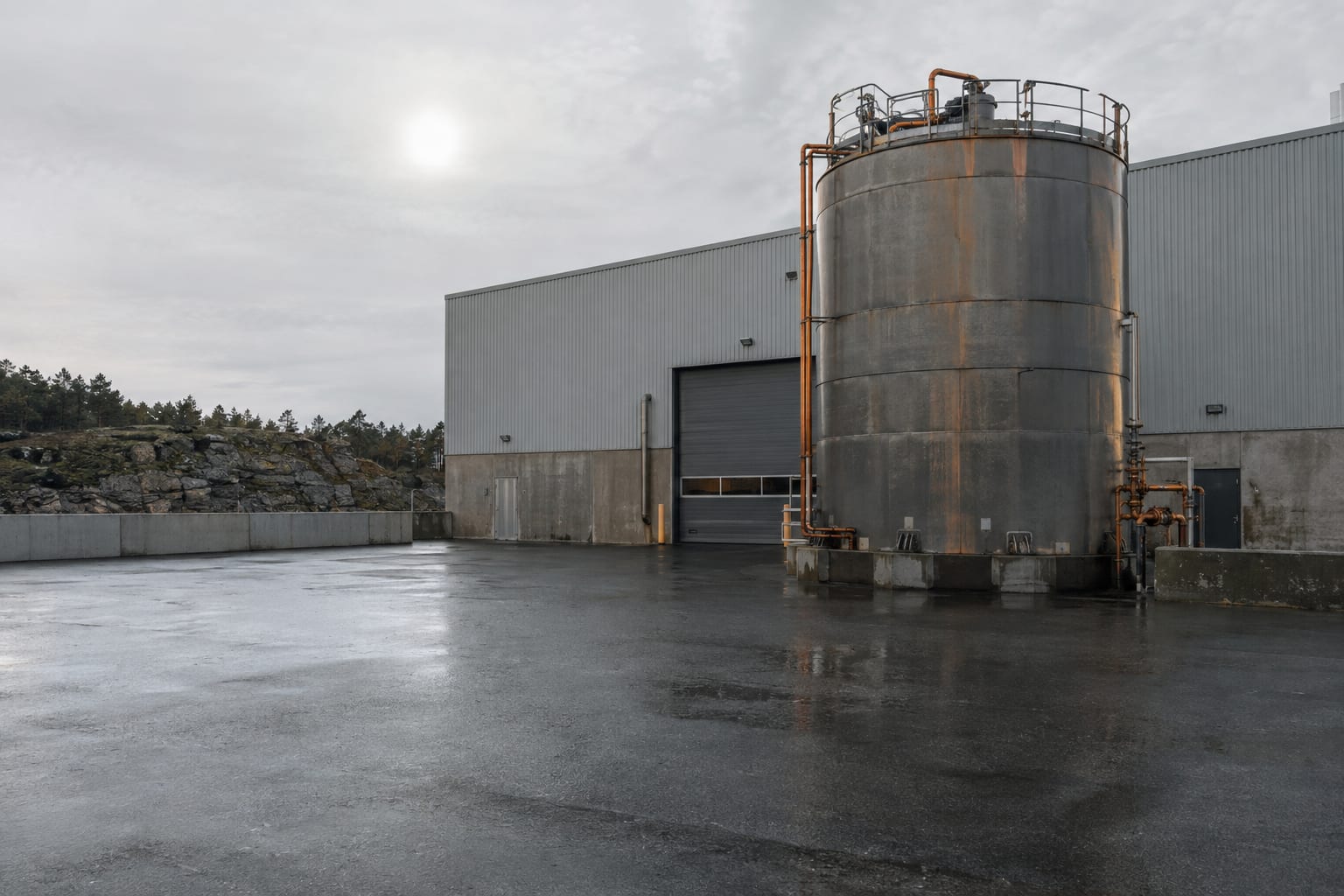 An oversized electrolyte tank stands on a loading apron outside an anonymous battery factory.