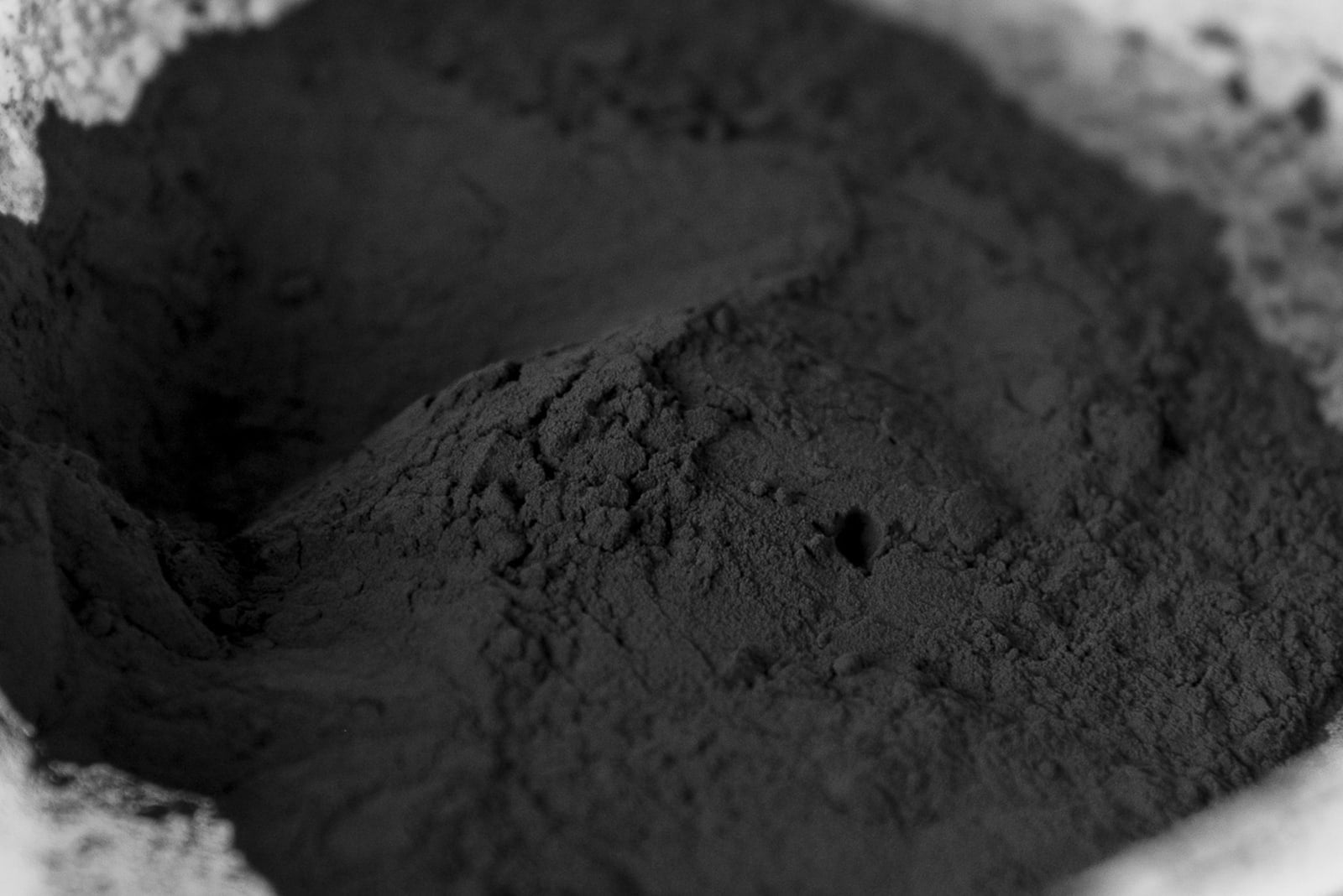 A close view shows dark granular recycled battery black mass in a product photograph.