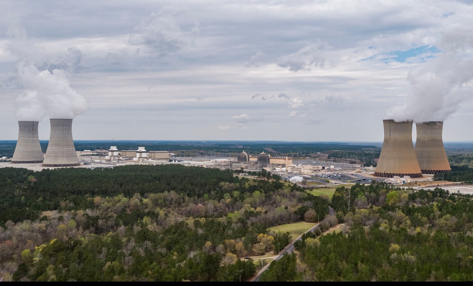 Aerial view of Plant Vogtle near Waynesboro, Georgia: four cooling towers steaming above the reactor buildings and the pine forest.