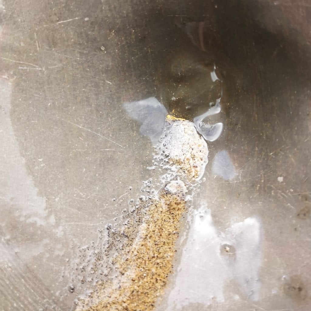 A pan contains visible gold from the Golden Hand target at Sela Creek.