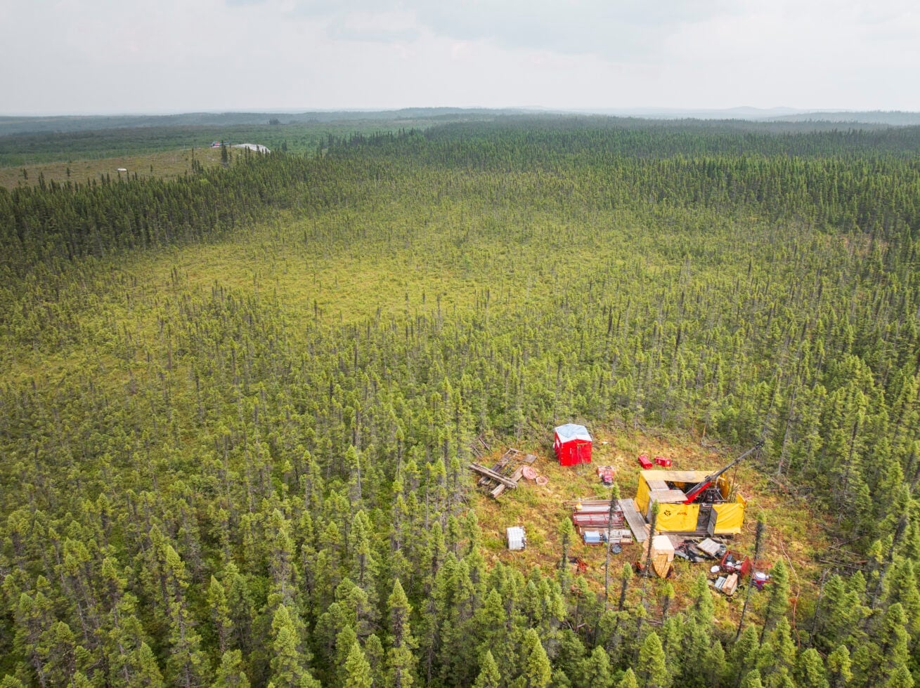 An aerial photograph shows a drill rig in a forest clearing at the Cisco Lithium Project.