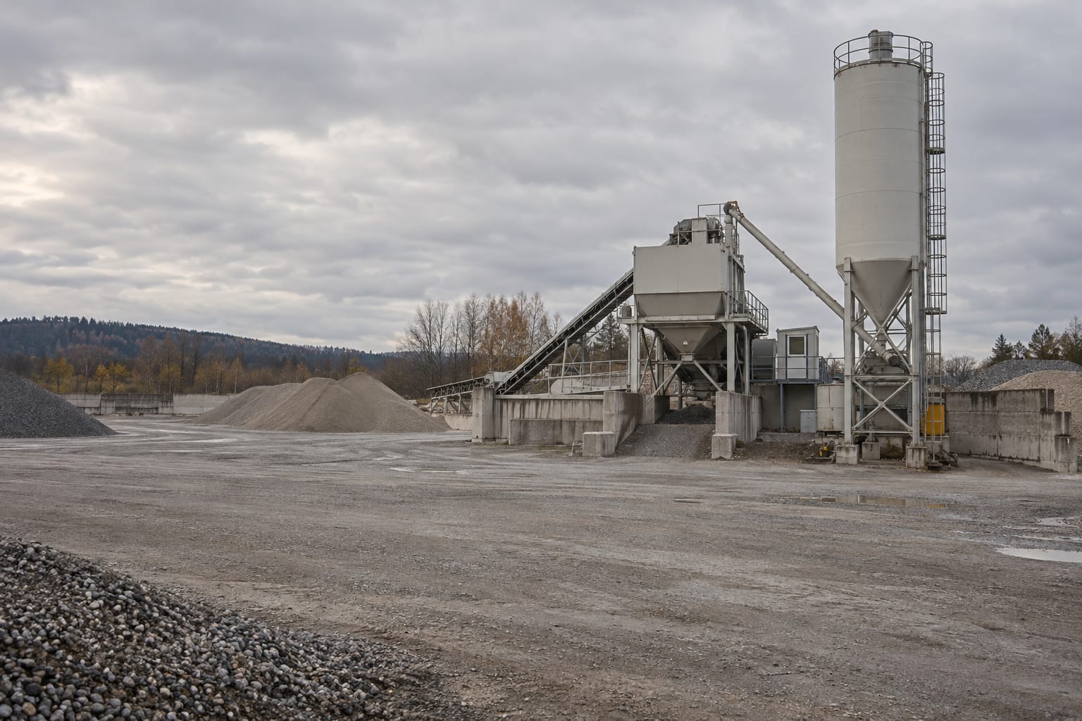 A portable concrete batch plant stands in an anonymous aggregate depot under an overcast sky.