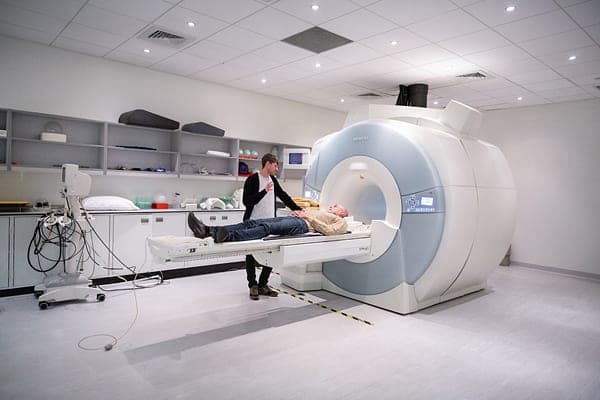 Robin Carhart-Harris (standing) and Michael Pollan at a functional magnetic resonance imaging machine at the Imperial Centre for Psychedelic Research