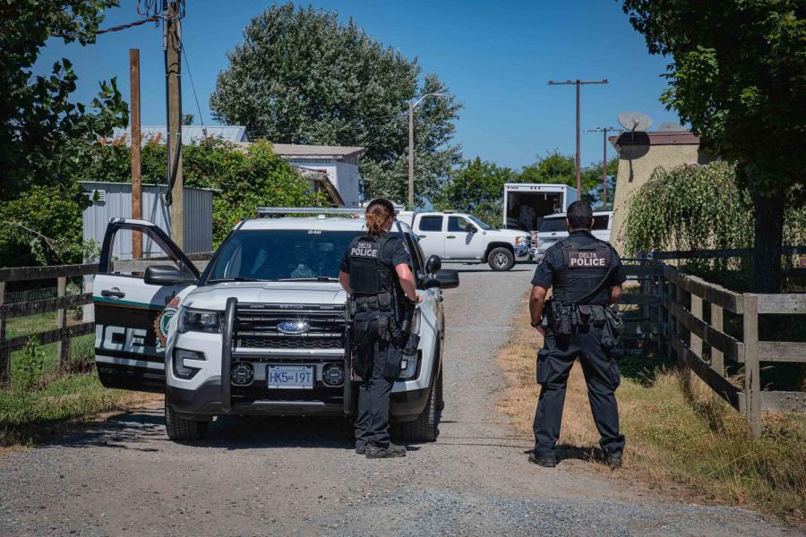 Two Delta police officers standing with their backs turned near a police cruiser