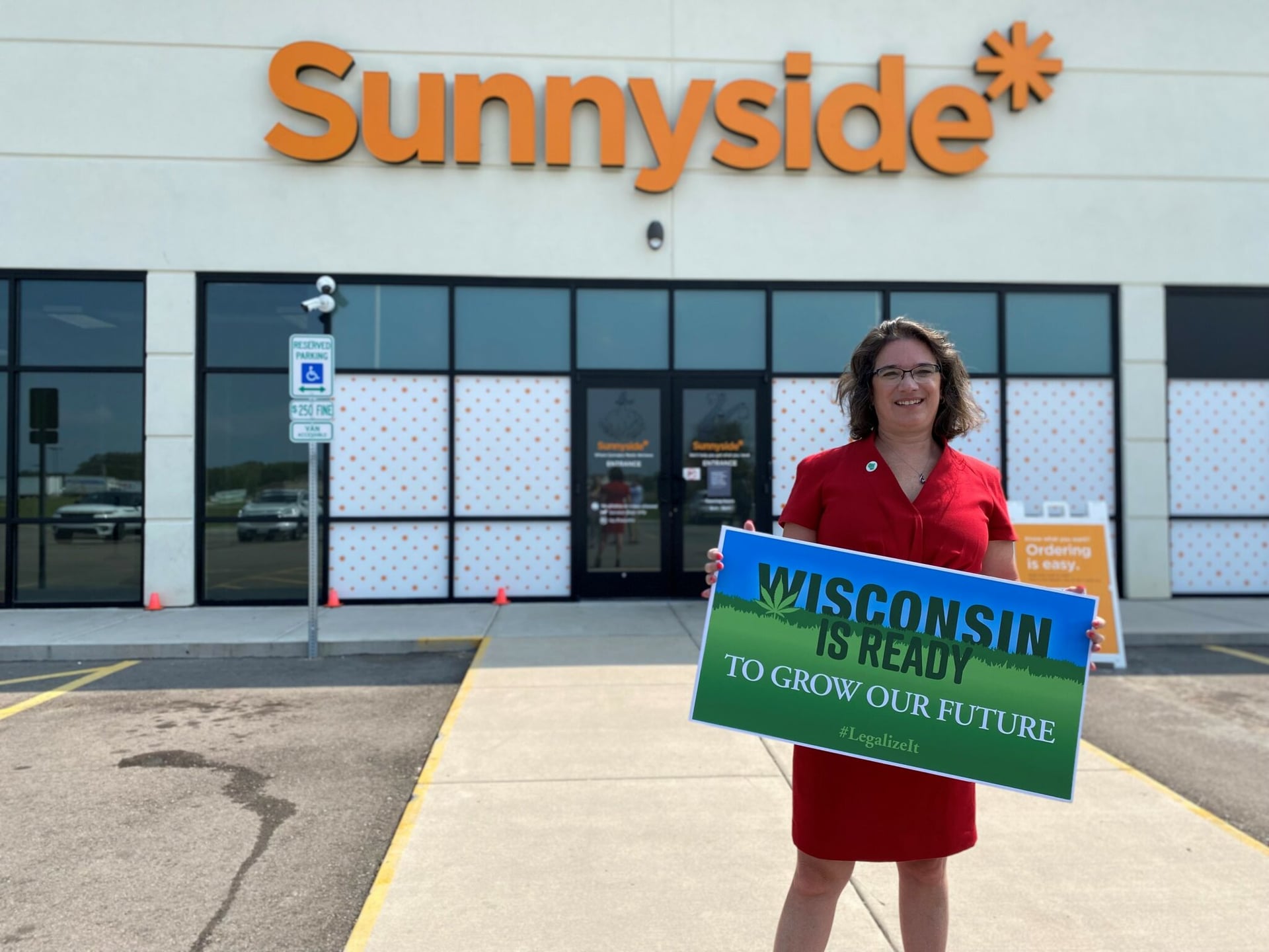 Sen. Melissa Agard standing outside an Illinois dispensary holding a sign saying, 'Wisconsin is ready'