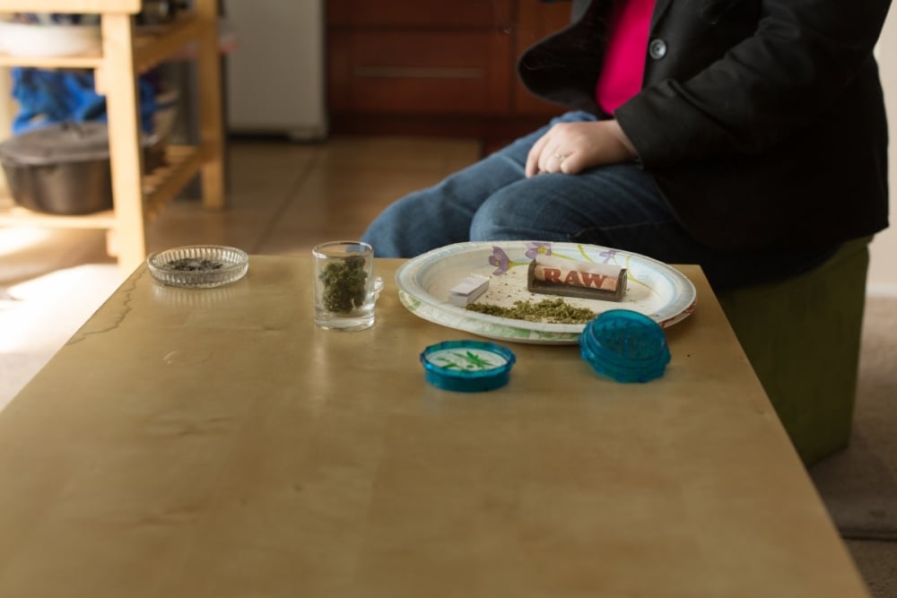 Person sitting at a kitchen table with cannabis and rolling papers out