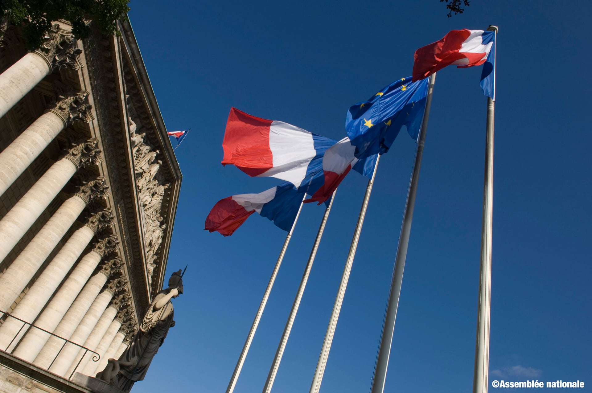 3 French and 1 EU flag waving in the air and the National Assembly building in the background