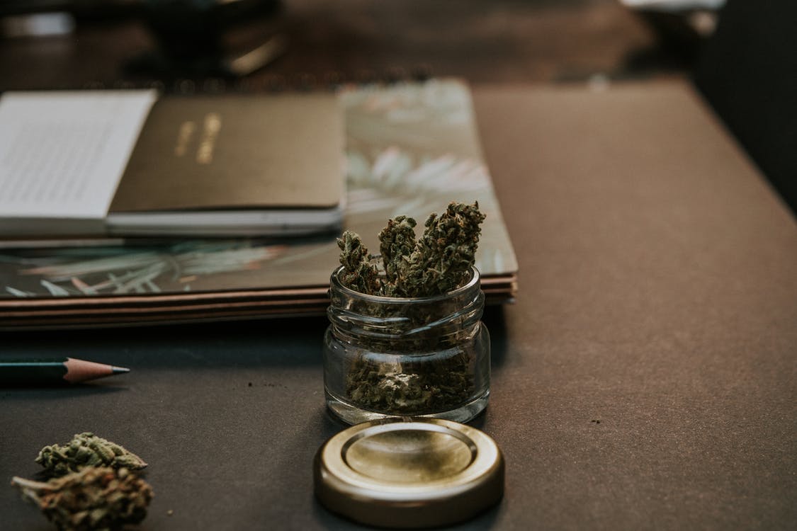 Cannabis is small jar next to a stack of notebooks
