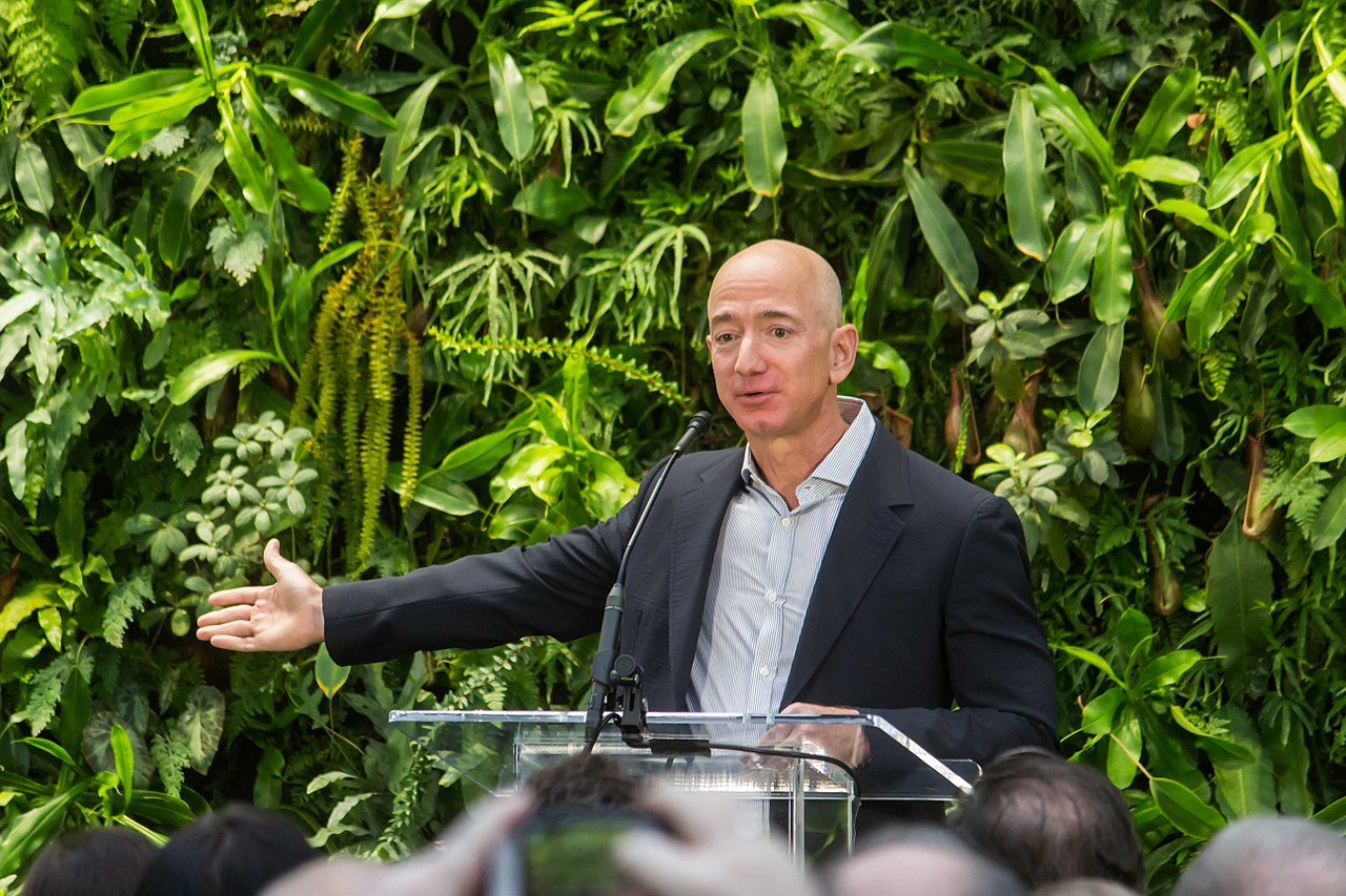 Amazon founder Jeff Bezos speaking in front of a wall of plants and leaves